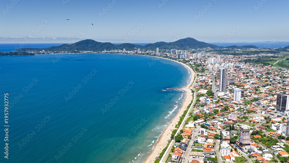 Fototapeta premium Aerial coastal view of Penha with curved shoreline, blue ocean, and dense urban area in Brazil.