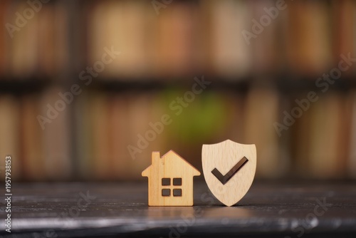 A small wooden house figure next to a shield icon representing home insurance and property security