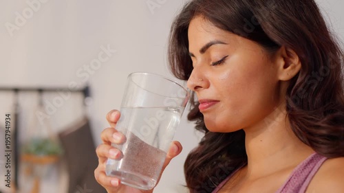 Attractive Indian woman drinking a glass of water in kitchen at home.