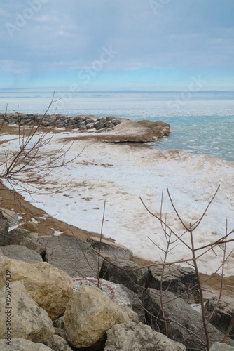 Frozen Shoreline On A Rocky Beach With Snow And Ice Under Overcast Winter Sky