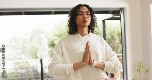 Non-binary person starting meditation pressing palms and breathing on balcony in hoodie, smartwatch