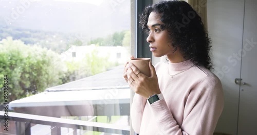 Non-binary person standing at window, cradling ceramic mug and sipping while reflecting, copy space
