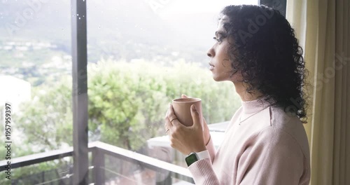 Person drinking coffee in pink sweater, smiling by sliding glass door