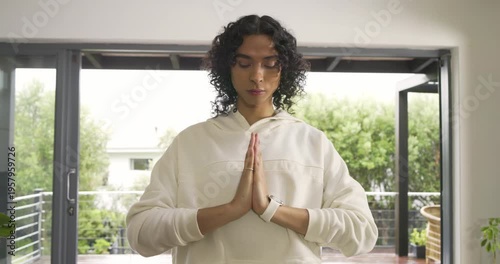 Non-binary person practicing meditation in prayer at sliding doors wearing smartwatch breathing