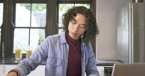 Non-binary person picking tote bag, writing notes, scrolling laptop and packing at kitchen table