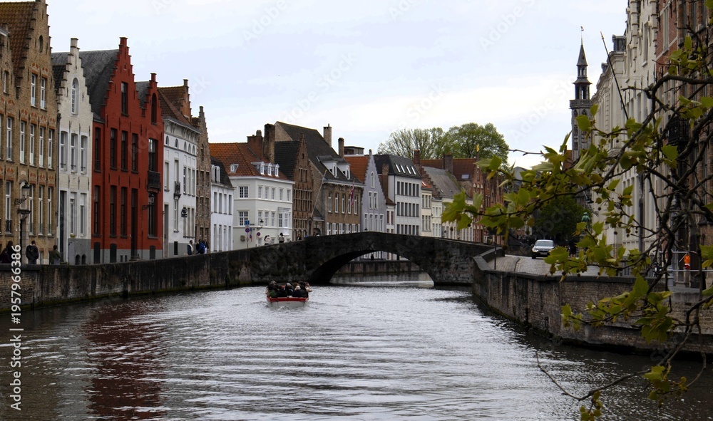 Obraz premium Tourist boat cruising through the historic canals of Bruges with ancient brick architecture and stone bridge