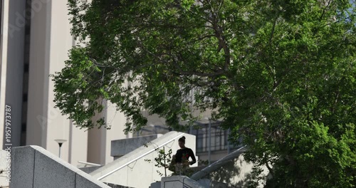 Campus concrete staircase is carrying commuters as single person is descending to plaza under tree