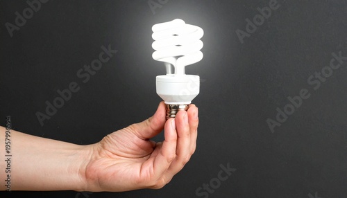 Hand holding glowing CFL bulb, spiral design, dark background