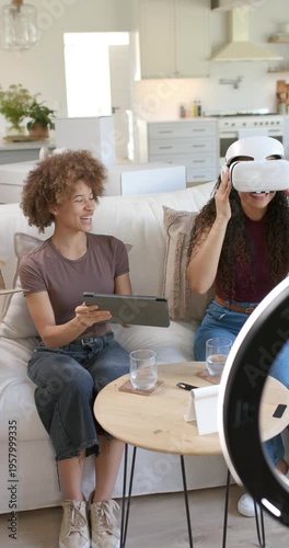 Vertical video: Female friends at home testing VR headset after seeing box, tablet filming reaction