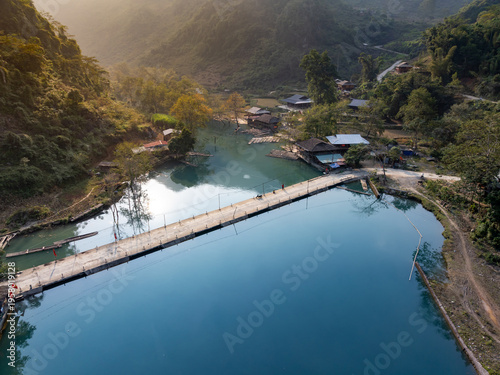 Fotografia A person walks a motorbike across a bridge in the rural village of Hang Than Lim, Yen Minh, Ha Giang, Vietnam