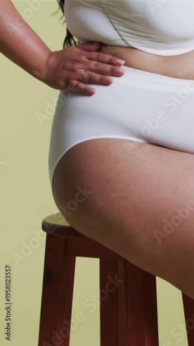 Vertical video: Camera panning up, model smoothing leg, fixing white set for studio shoot, smiling