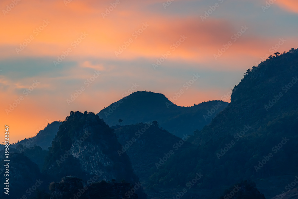 Obraz premium A scenic view of the silhouette of mountains against a colorful sky at dusk in TDong Van, Ha Giang, Vietnam. The landscape is serene and peaceful.