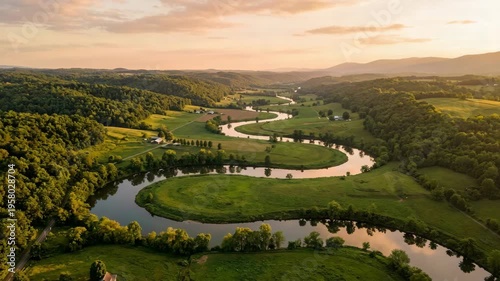 Serpentine river winding through lush green valleys and rolling hills at sunrise