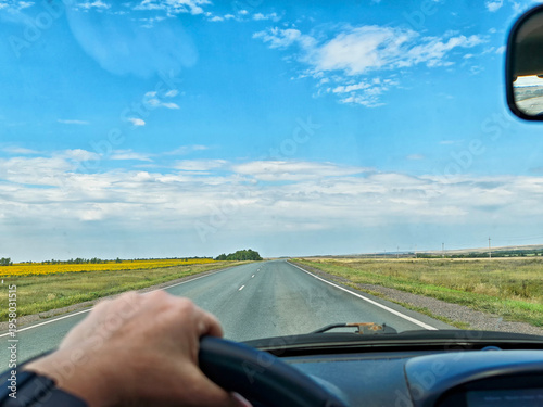 Fotografie Driving on a road through fields on a cloudy autumn day while holding the steeri