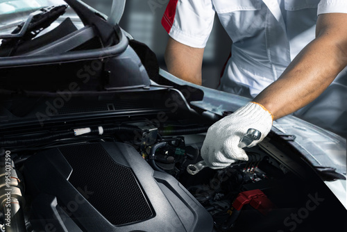 Foto Close-up of a professional car mechanic wearing gloves using a wrench to inspect and maintain a vehicle engine in an auto repair garage