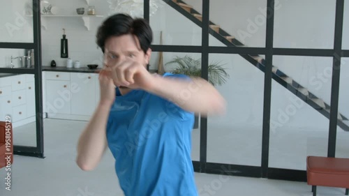 Portrait of active sporty muscular build man practicing shadow boxing workout, training punching techniques, improving upper and lower body muscles at home.