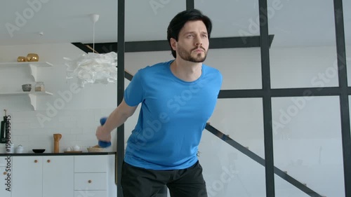 Portrait of active fit man practicing dumbbell triceps kickback exercise, strengthening and toning arm muscles while doing weight training workout indoors.