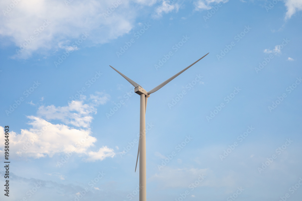 Fototapeta premium Single wind turbine against clear blue sky with soft clouds, minimal composition highlighting renewable energy and clean power generation in modern sustainable environment.