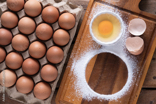Top-view of fresh eggs in a carton baking preparation setup on a wooden board.