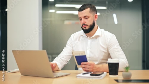 Man focused on laptop, holding passport and ticket. Actively planning travel, appearing serious and absorbed in the online booking process. Represents preparation, anticipation for upcoming journeys.