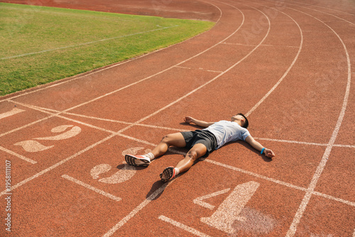 Φωτογραφία Athlete lying on the track resting and recovering after a long run showing exhau