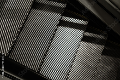 Close-up of escalator steps forming strong diagonal lines and repetitive metallic texture, creating an abstract pattern with light and shadow contrast
