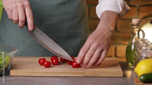 A male chef picks tomatoes from the vine and cuts them into halves to prepare a salad.