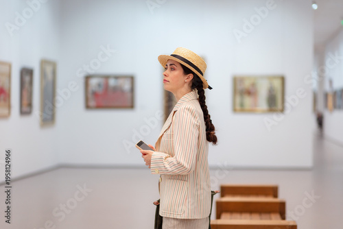 Foto Side shot of adult Caucasian elegant woman in straw hat and suit contemplating artwork in the art gallery