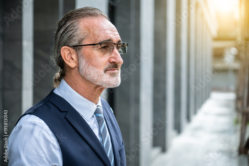 Serious mature Caucasian businessman looking sideways thoughtful expression wearing eyeglasses formal suit standing outdoor in modern city
