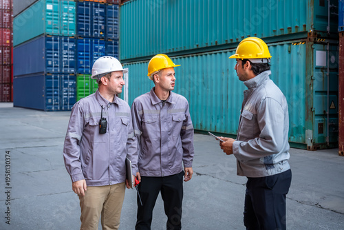 Engineer industrial workers males discussing logistics operations in shipping container yard with safety helmets