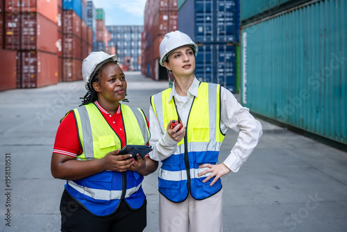Female industrial workers engineer inspecting shipping container logistics with safety gear and radio communication