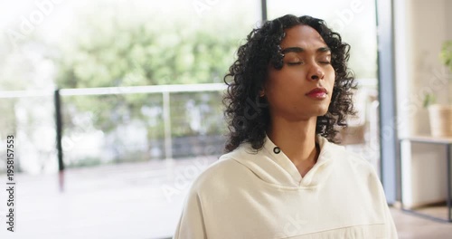 After sitting, non-binary adult inhaling holding breath then exhaling beside glass door and plant