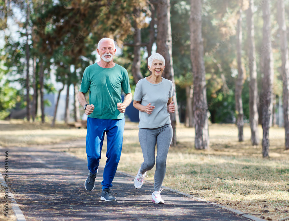 Obraz premium Smiling active mature senior couple jogging together in the park
