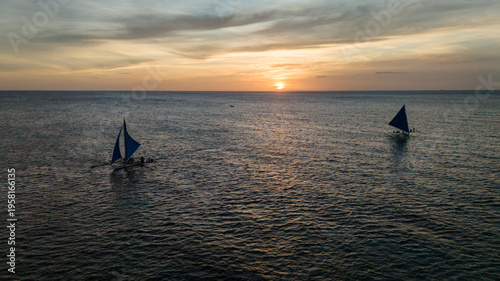 Картината върху платно Aerial view of traditional Paraw sailboats sailing on the calm ocean at sunset in Boracay, Philippines