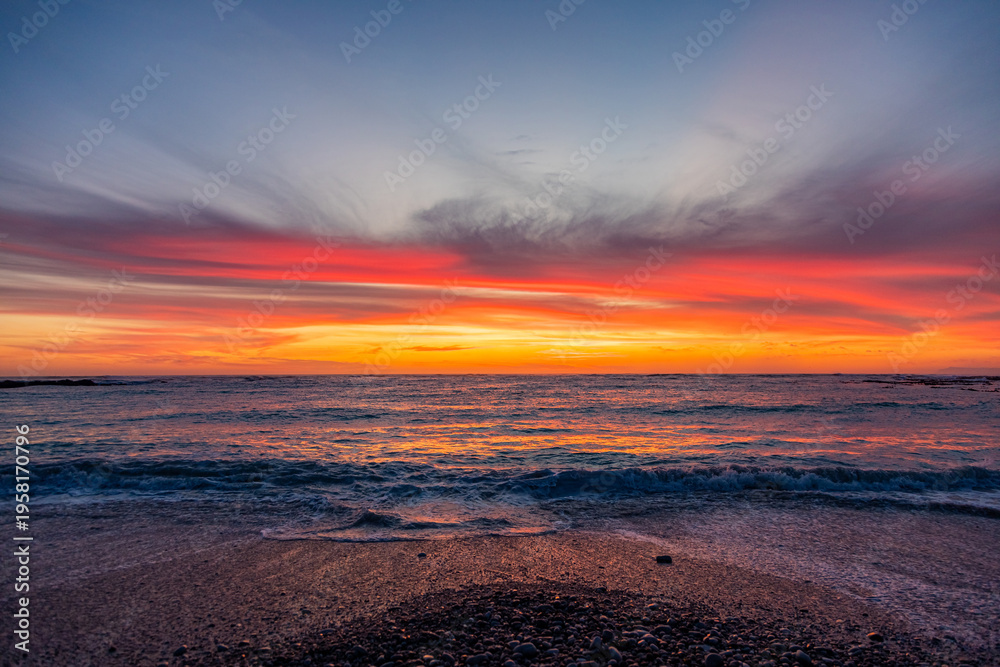 Obraz premium Dramatic Golden sunset over tranquil beach, waves lashing the pebble coastline