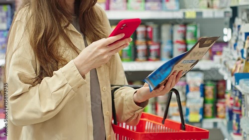 Woman choosing pet food before purchase with smartphone, comparing price, rating and reviews product, mobile assisted shopping in pet shop or supermarket