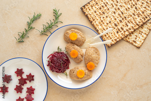 Jewish holiday food background with gefilte fish, bitter herbs maror, matzah, rosemary on ceramic surface.
