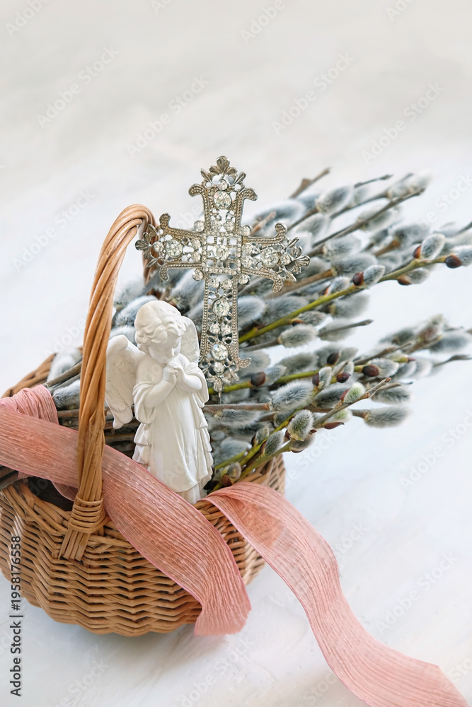 Fototapeta premium Palm Sunday background. wicker basket with pussy willow branches, christianity cross and angel figurine on light table. Easter, Palm Sunday holidays. prayer, faith, orthodox Church, religion concept.
