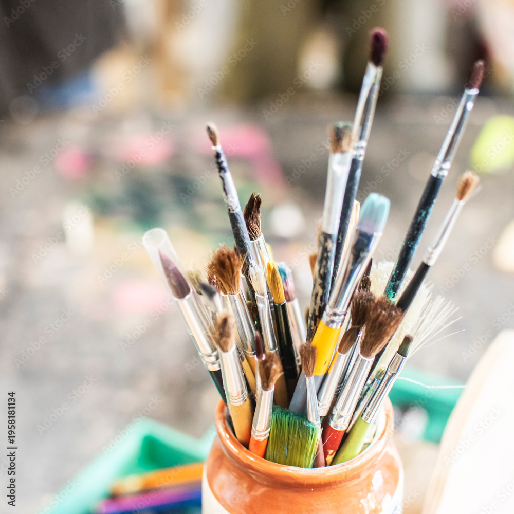 Fototapeta premium Collection of used paint brushes stored in a jar on a worktable in an art workshop. Creative workspace with painting tools used for crafts, art projects and hobby activities.