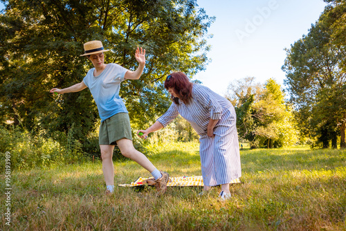 Middle-aged woman and her young daughter in a summer park using insect repellent to prevent bites from mosquitoes and ticks while relaxing together outdoors. Mid shot