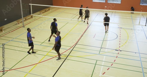 Left male team blue shirts reacting to gray team serving, receiving and defending volleyball in gym