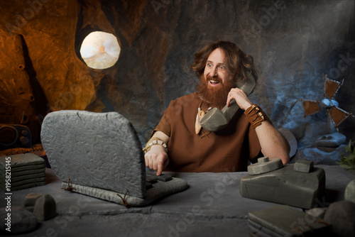 Fotografija Overworked caveman office clerk sitting at a stone desk surrounded by piles of prehistoric stone documents