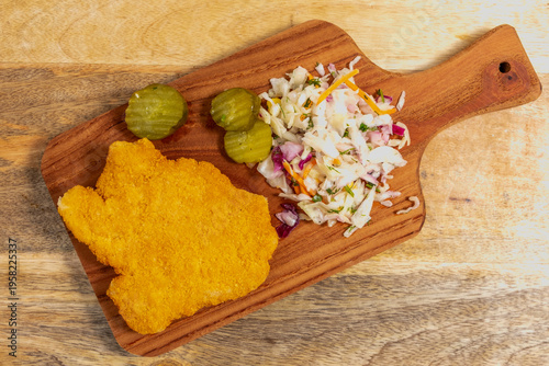 Food ideas for tasty snack. Chicken schnitzel, sauerkraut, pickled cucumber on wooden platter. Top view.
