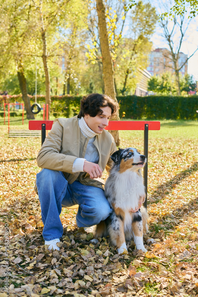Fototapeta premium Young man enjoys a sunny spring day with his Australian Shepherd in the park