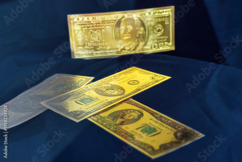 Golden souvenir one hundred dollar banknotes scattered on a dark blue fabric background.