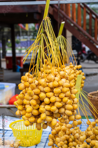 Bunches of fresh yellow Barhi dates hanging on a rack at a local fruit market stall.