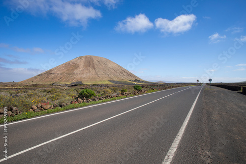 An empty, straight road in Lanzarote, with a hill or volcano visible on the right.
