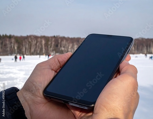 Person Holding a Smartphone in a Snowy Landscape.