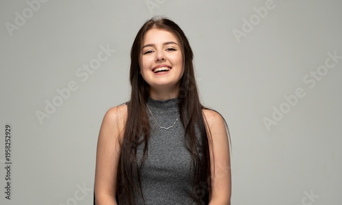 Young woman confidently smiling and laughing, expressing happiness and cheerful emotion while posing in a studio