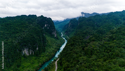 Aerial view of the winding river cutting through the lush, verdant valley beneath the brooding sky, Dark Cave, Qung Binh, Vietnam.